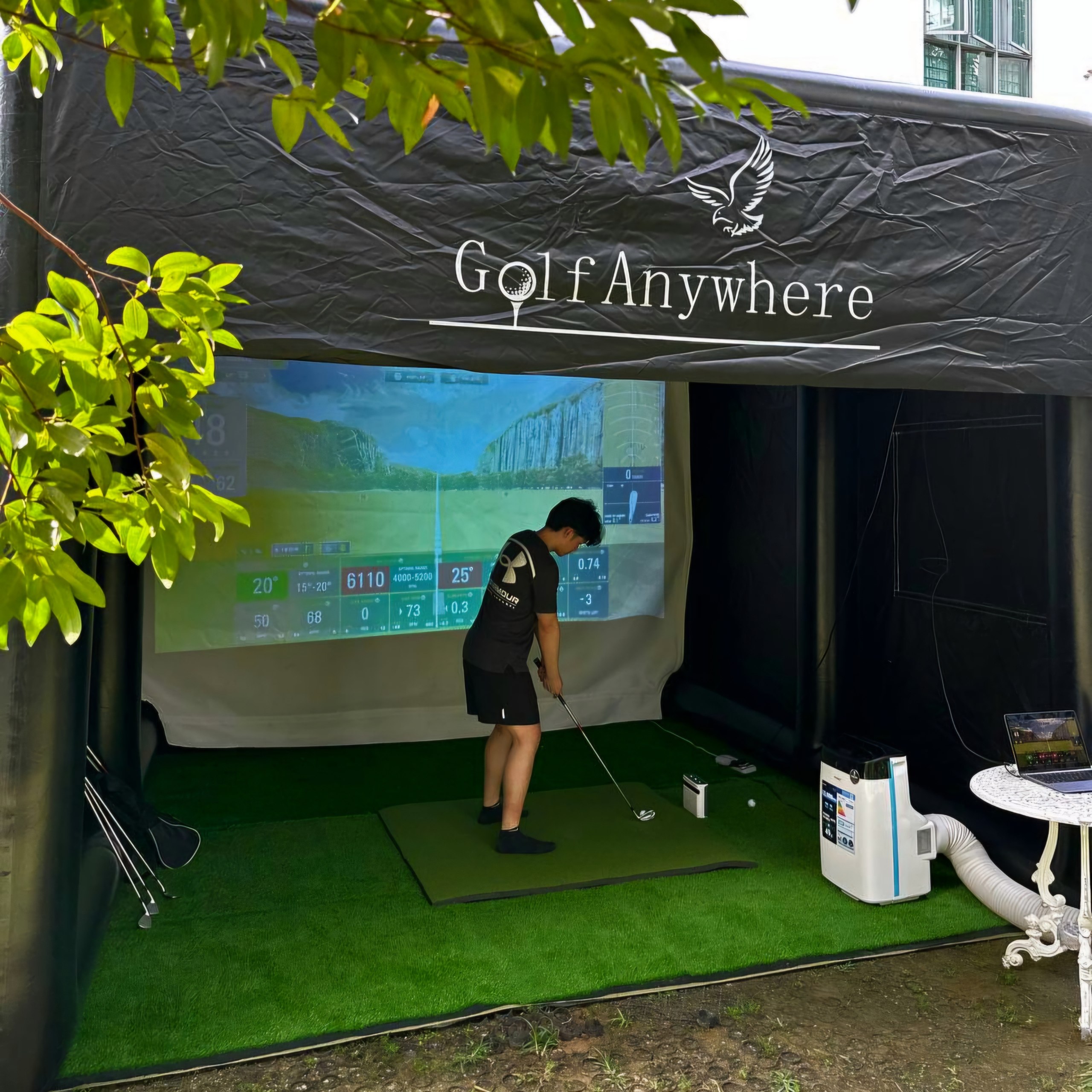 Golf Anywhere branded marquee tent with player in action, outdoor daytime setup